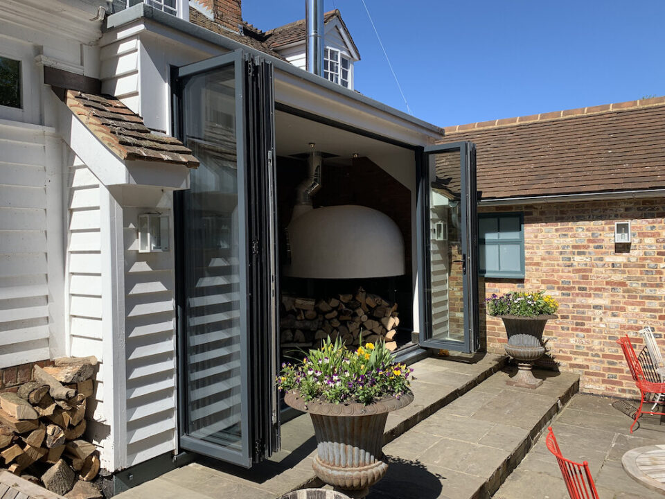 Grey aluminium bifold doors opening onto a courtyard with a log store