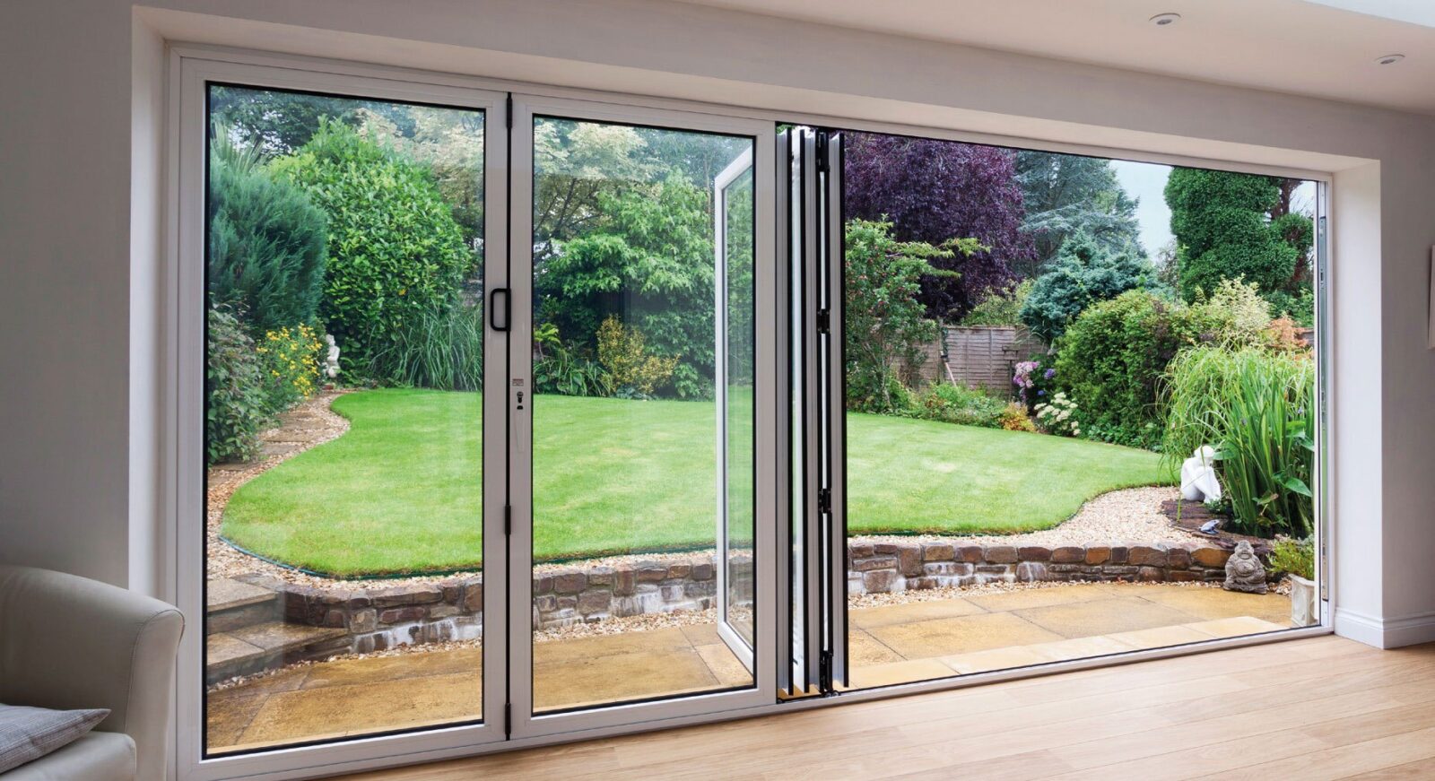White aluminium bifold doors folded open onto a lawned garden