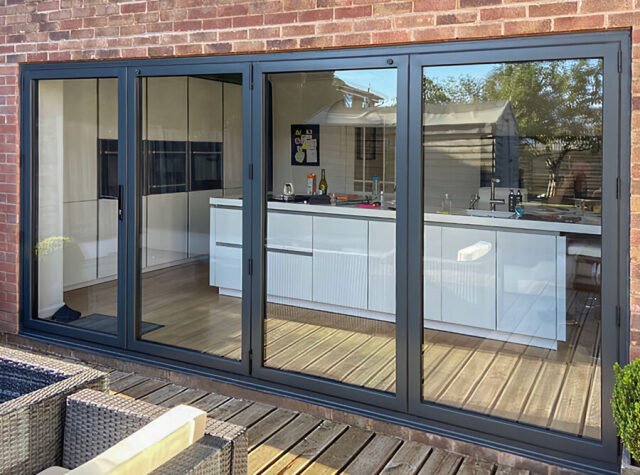 Grey aluminium bifold doors folded back from a kitchen to decking