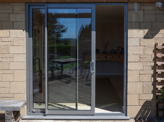 Grey aluminium sliding door in a stone wall opening onto a patio